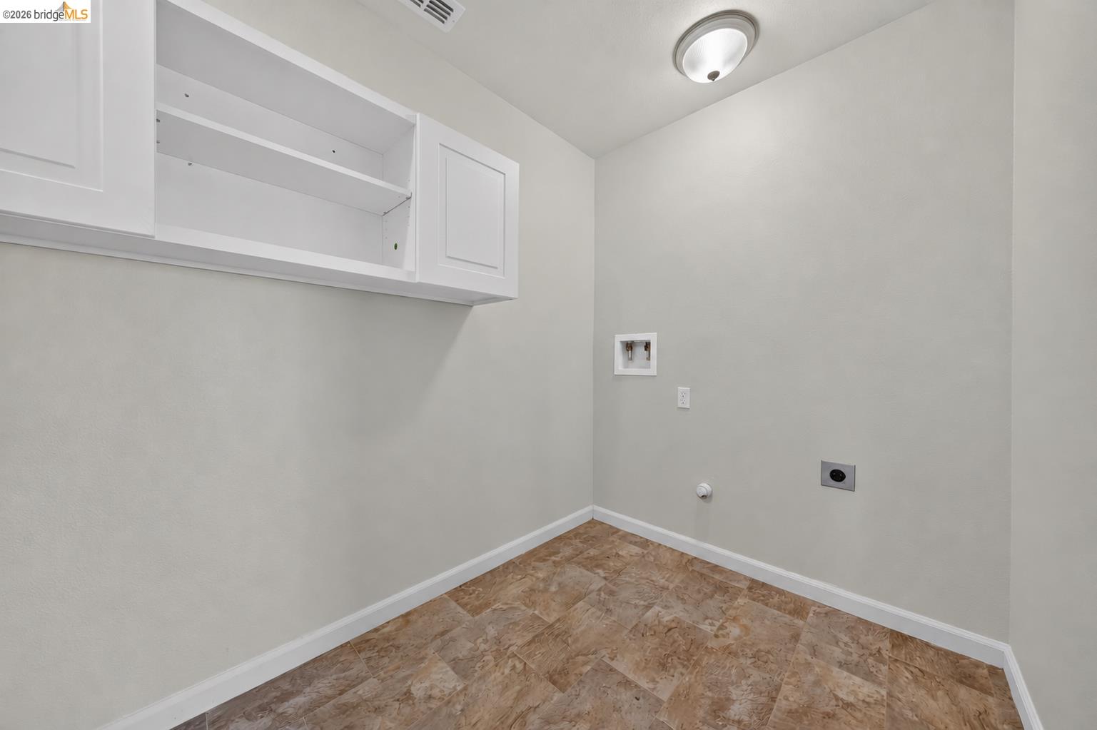 Laundry room with washer hookups, overhead cabinets, and brown tile flooring.