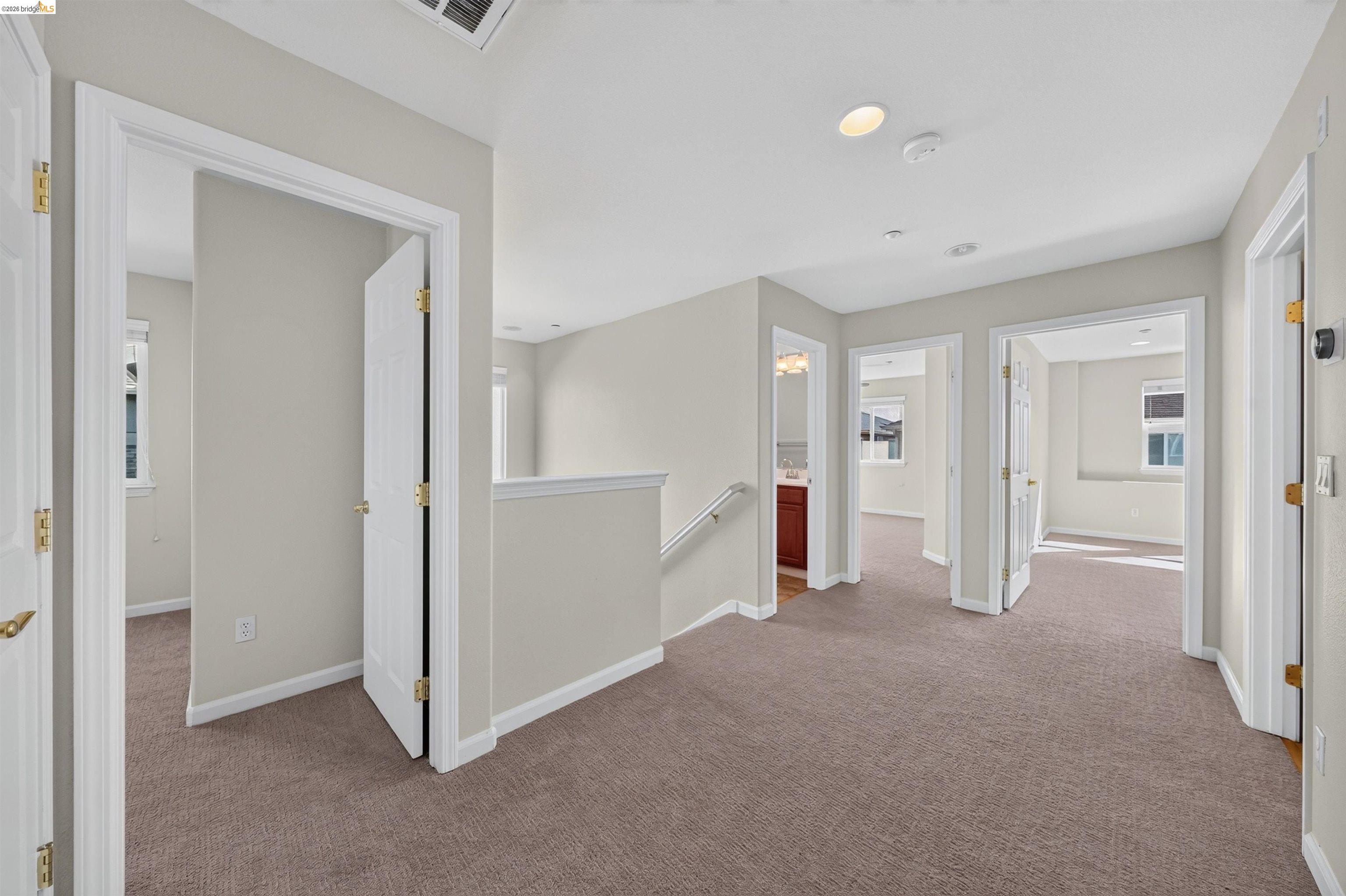 Carpeted upstairs hallway with multiple open doorways and a stair railing.