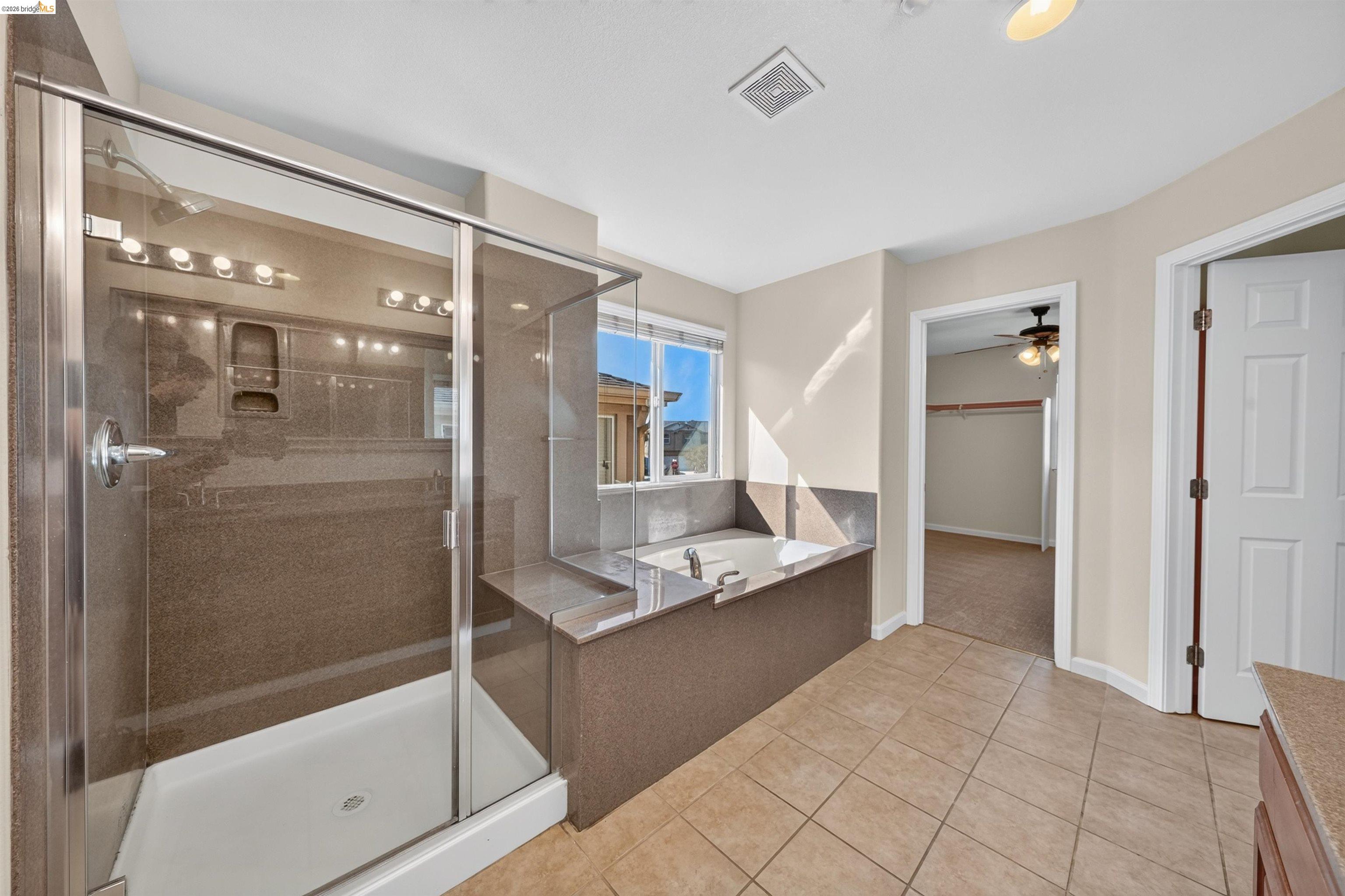 Bathroom with a glass-enclosed shower and built-in soaking tub beside a sunny window.