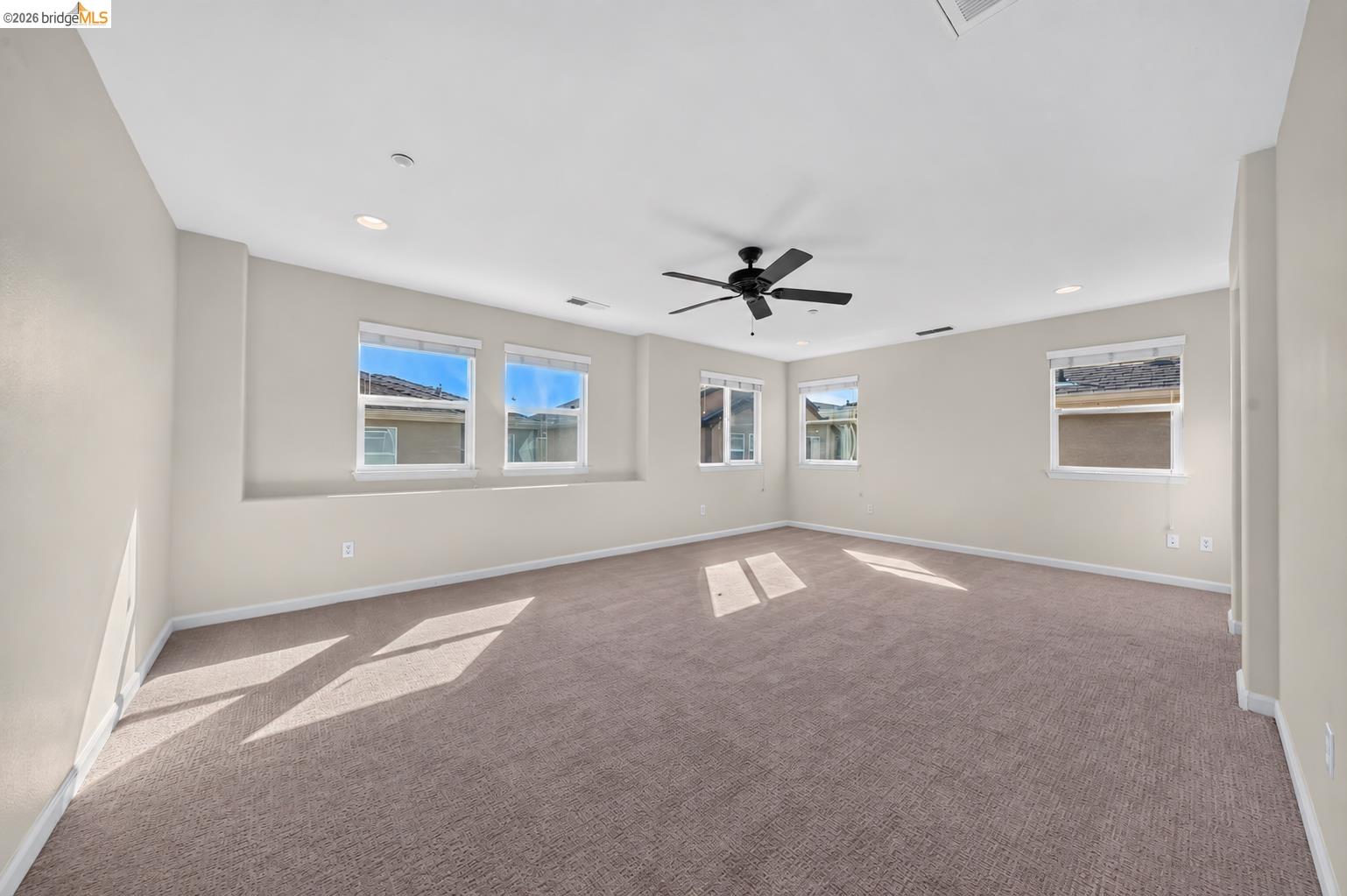 Empty carpeted room with several windows and a ceiling fan.