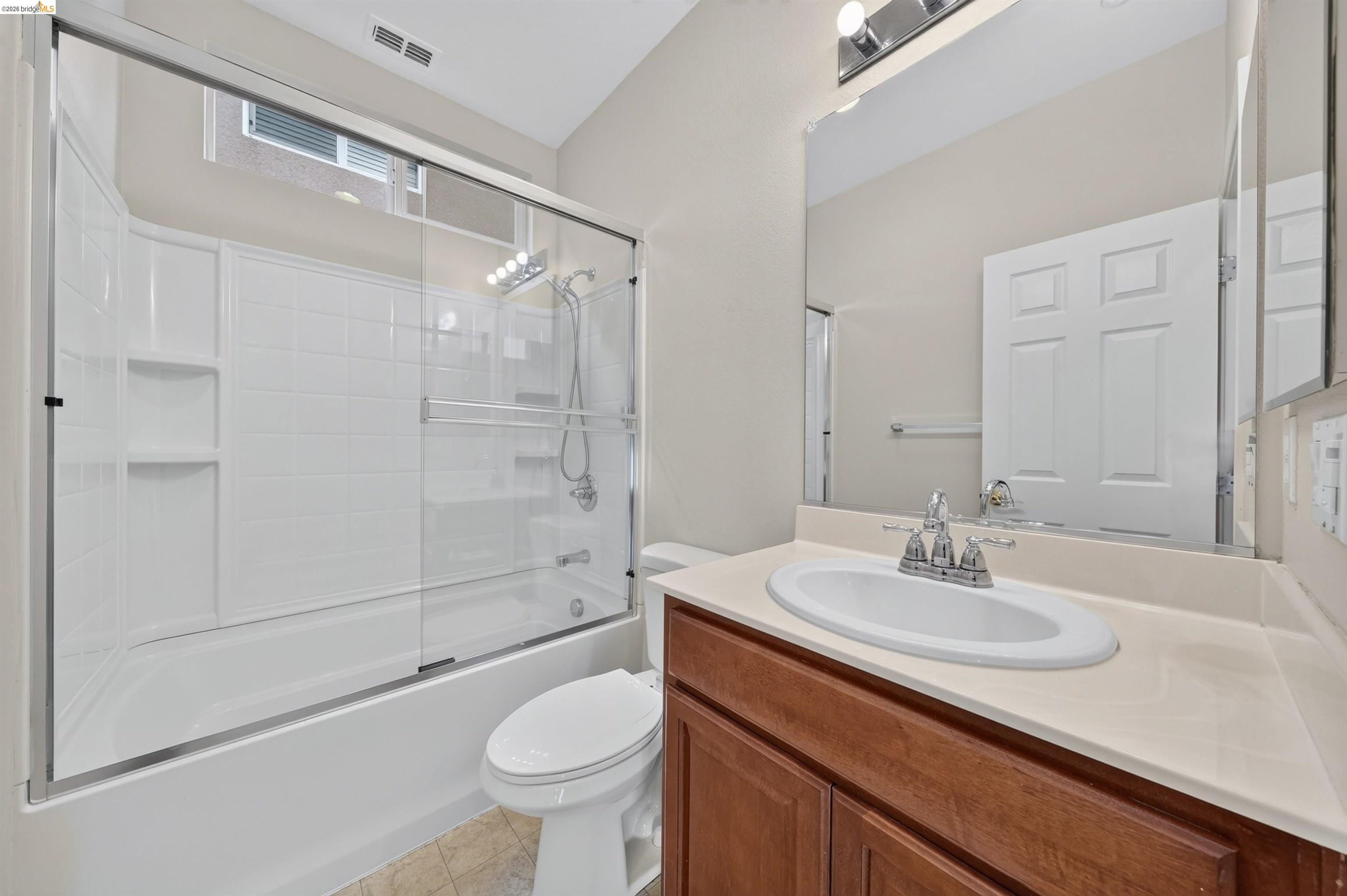 Bathroom with a glass-enclosed tub and shower beside a wood vanity.