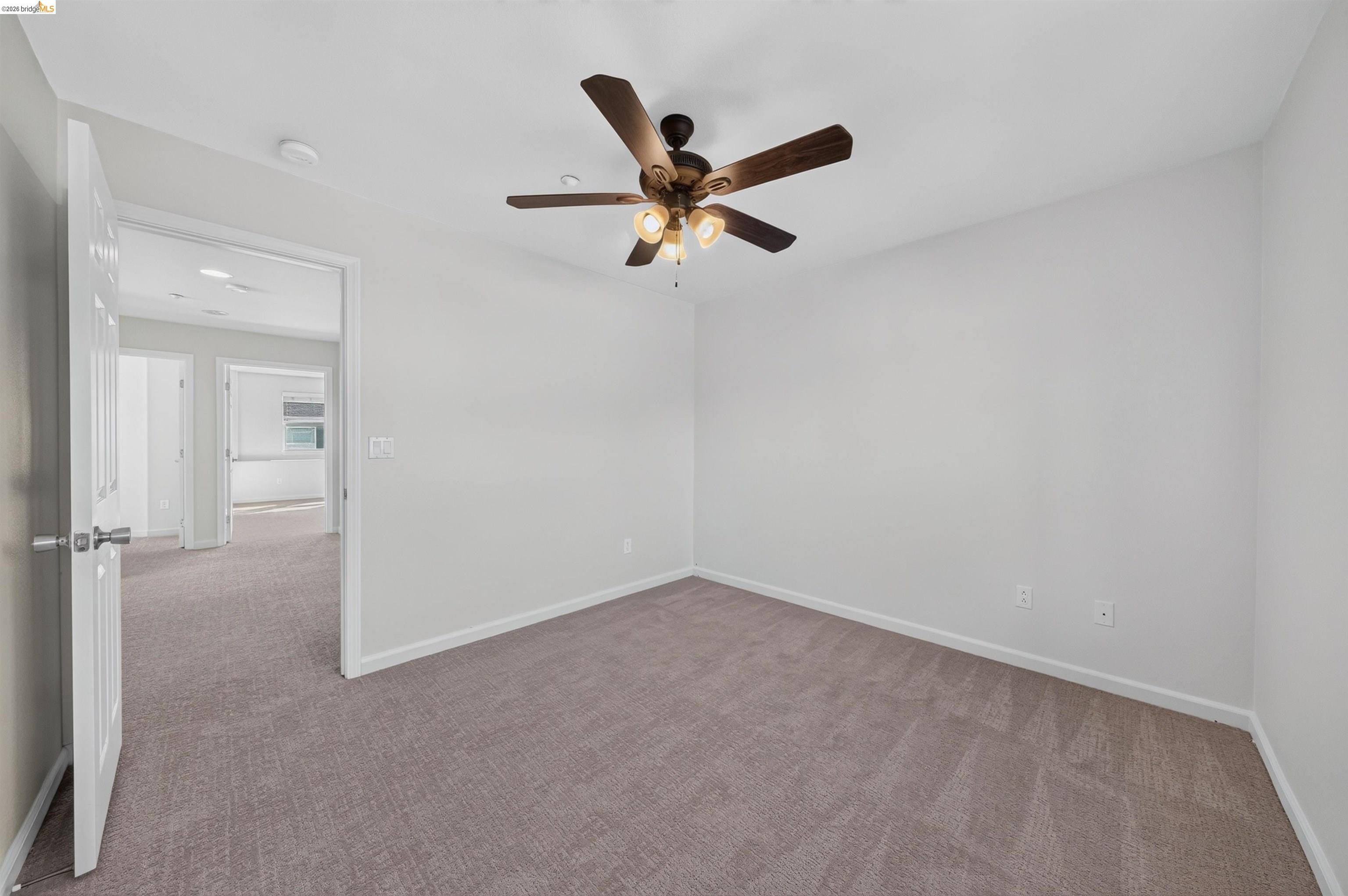 Empty carpeted room with a ceiling fan and open doorway to adjoining rooms.