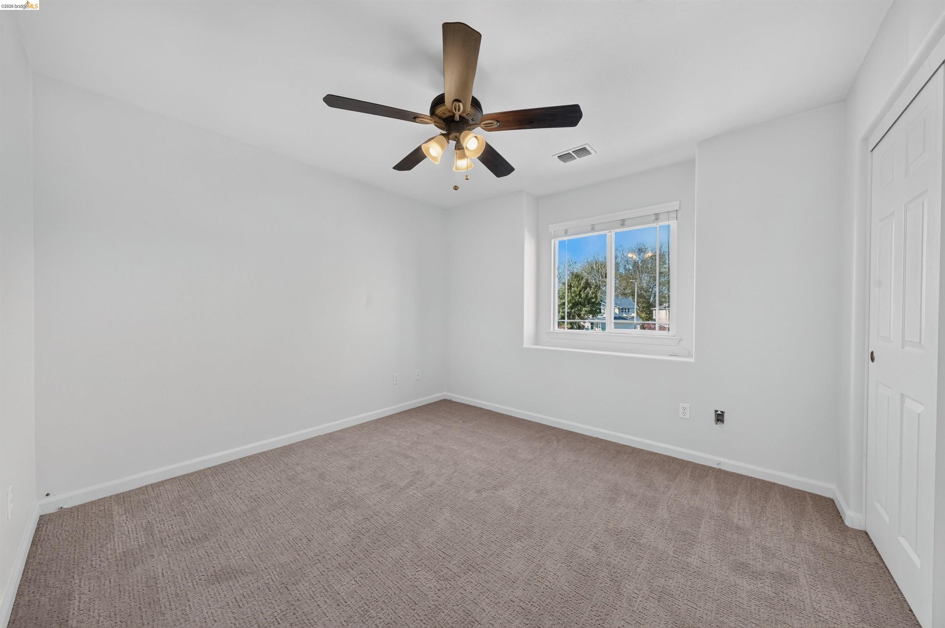 Empty carpeted bedroom with a ceiling fan, window, and closet.