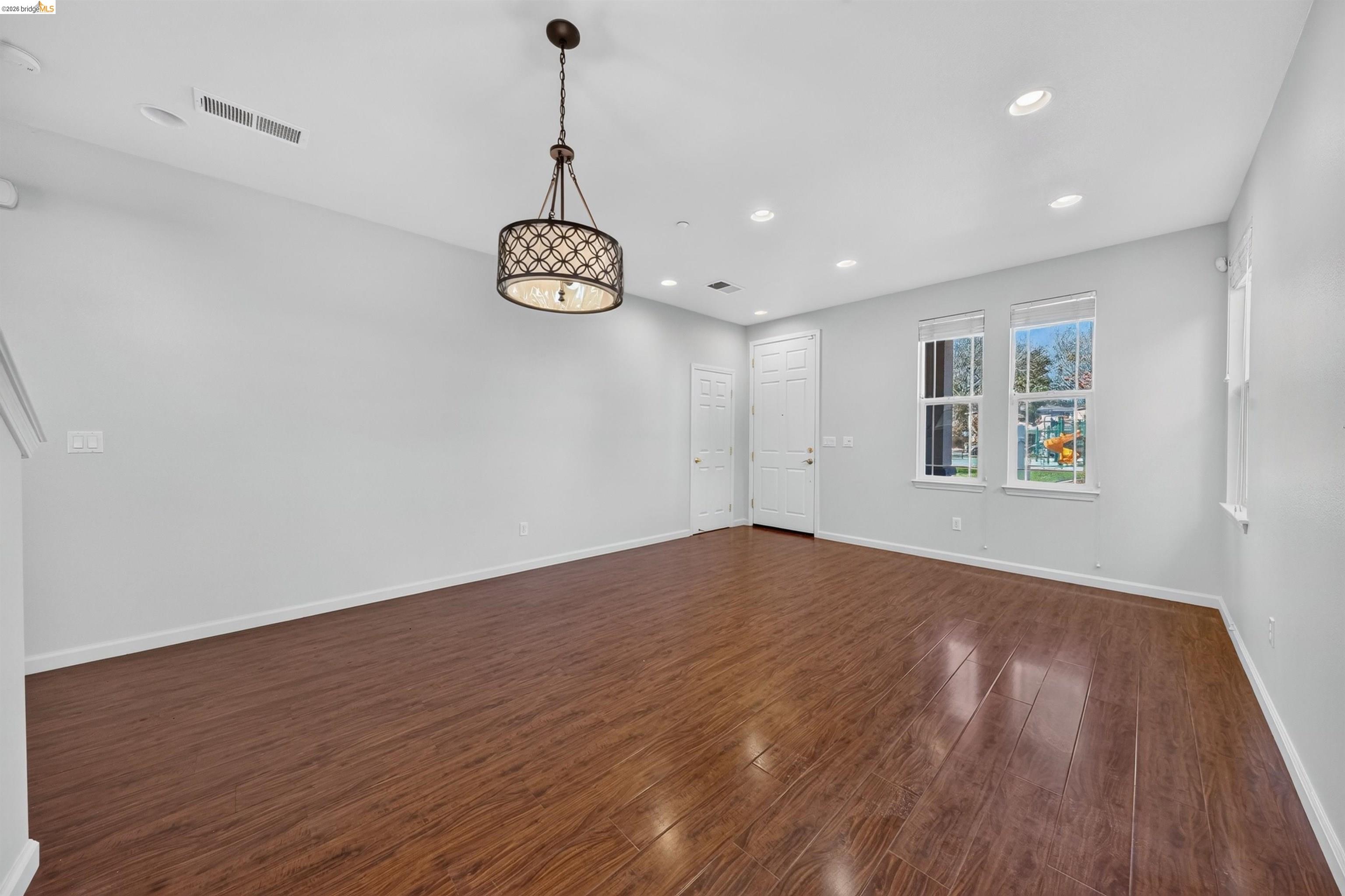 Empty room with glossy wood-look flooring, a decorative pendant light, and two windows.