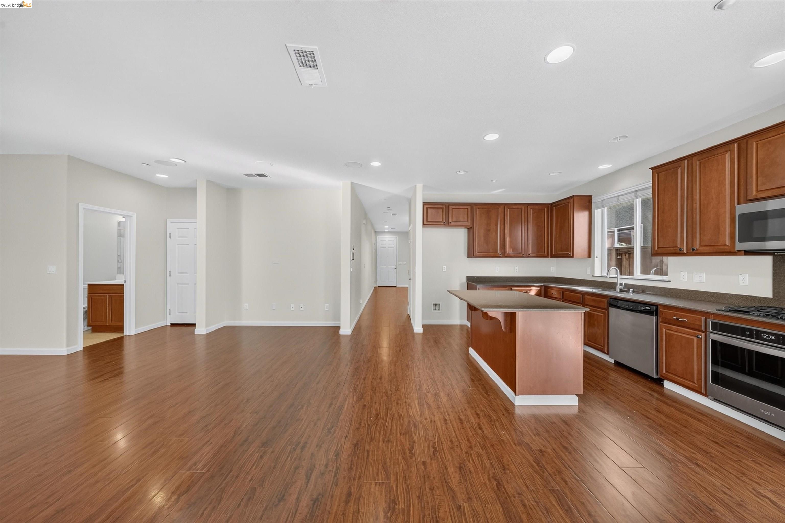 Open kitchen and living area with wood flooring, brown cabinets, and a central island.