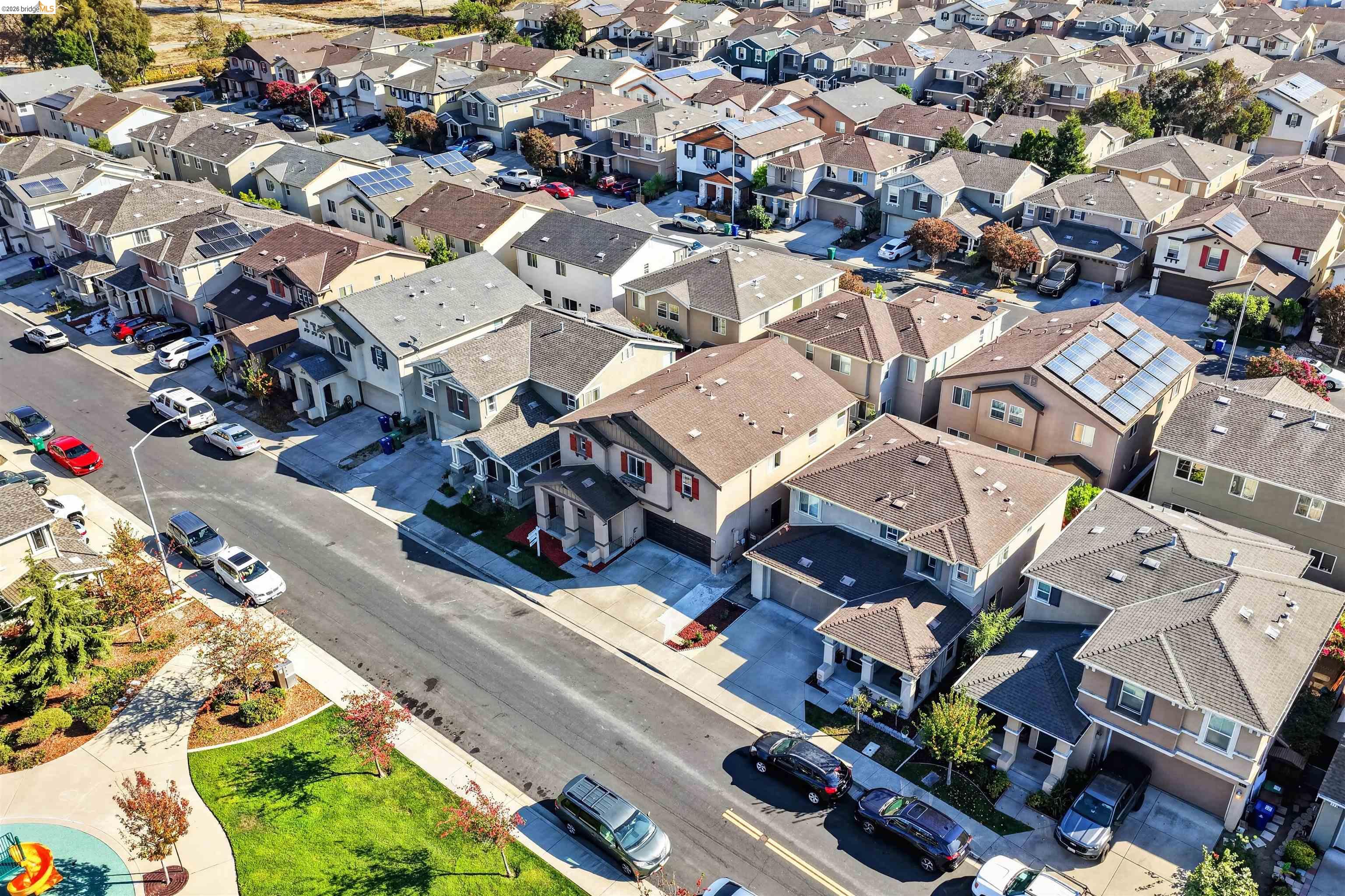 Aerial view of a residential neighborhood with rows of homes, solar panels, and a small park.