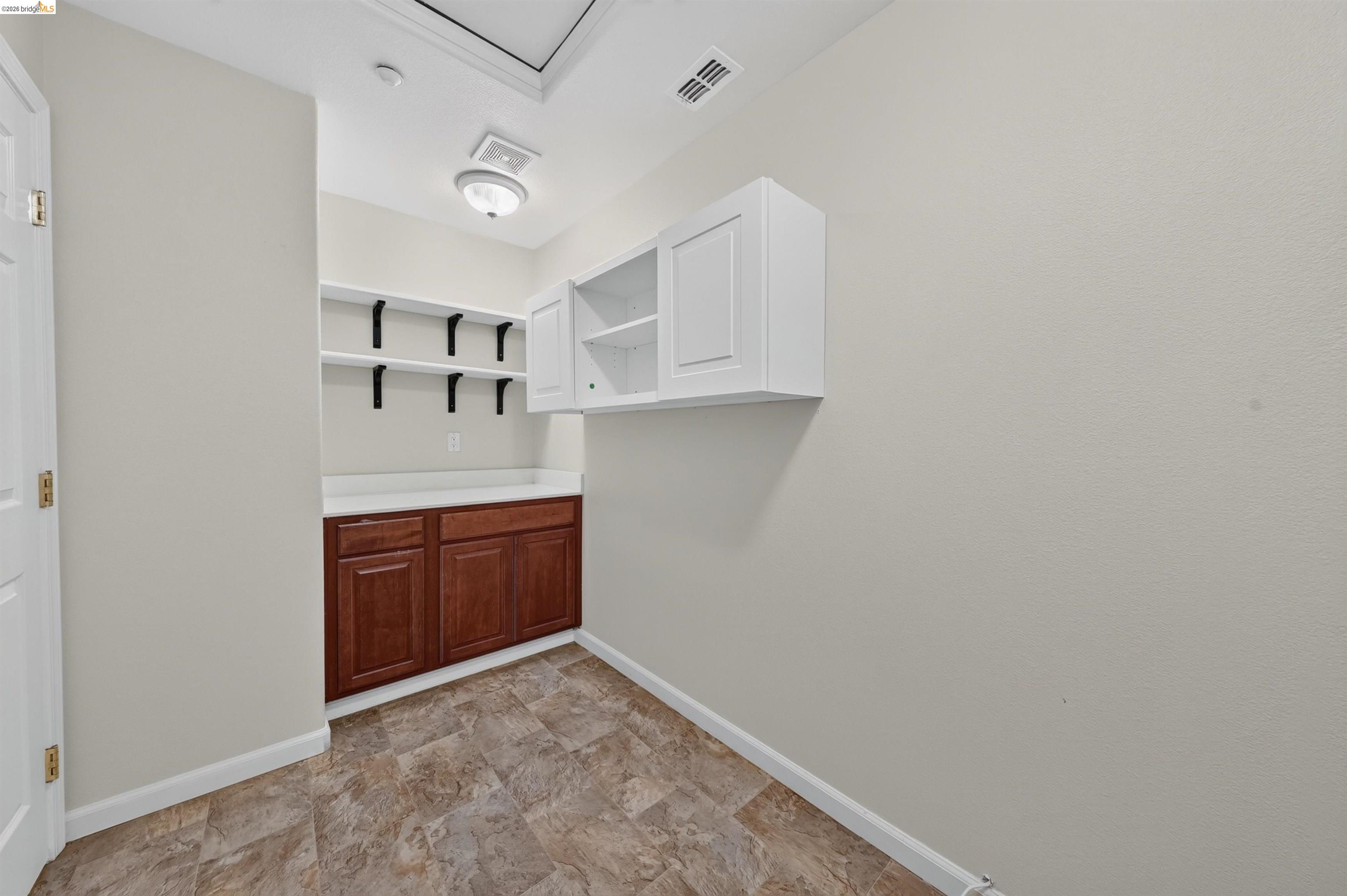 Laundry room with wall shelves, white upper cabinets, and reddish-brown lower cabinets.