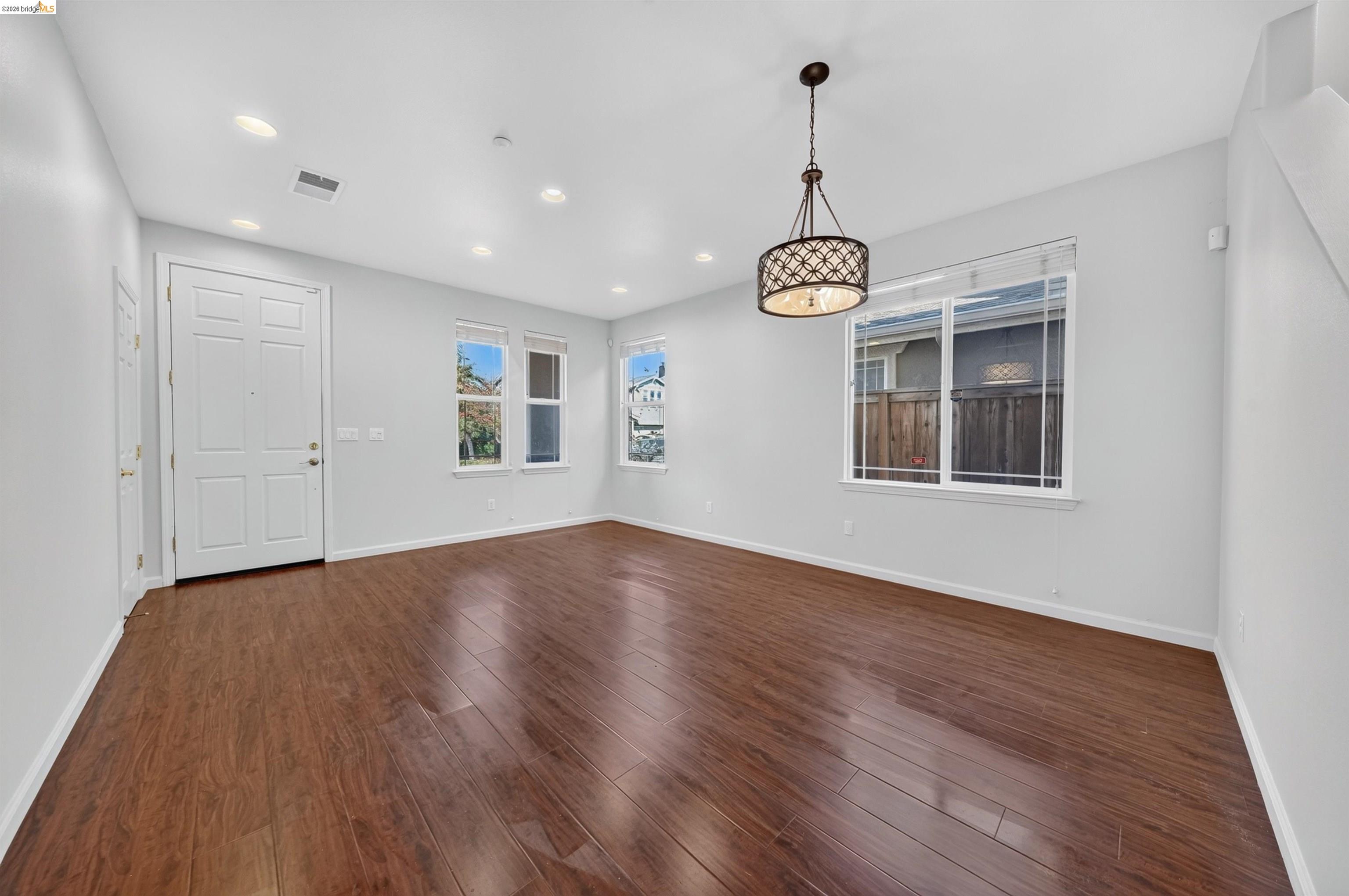 Empty room with dark wood flooring, white walls, and a decorative pendant light.