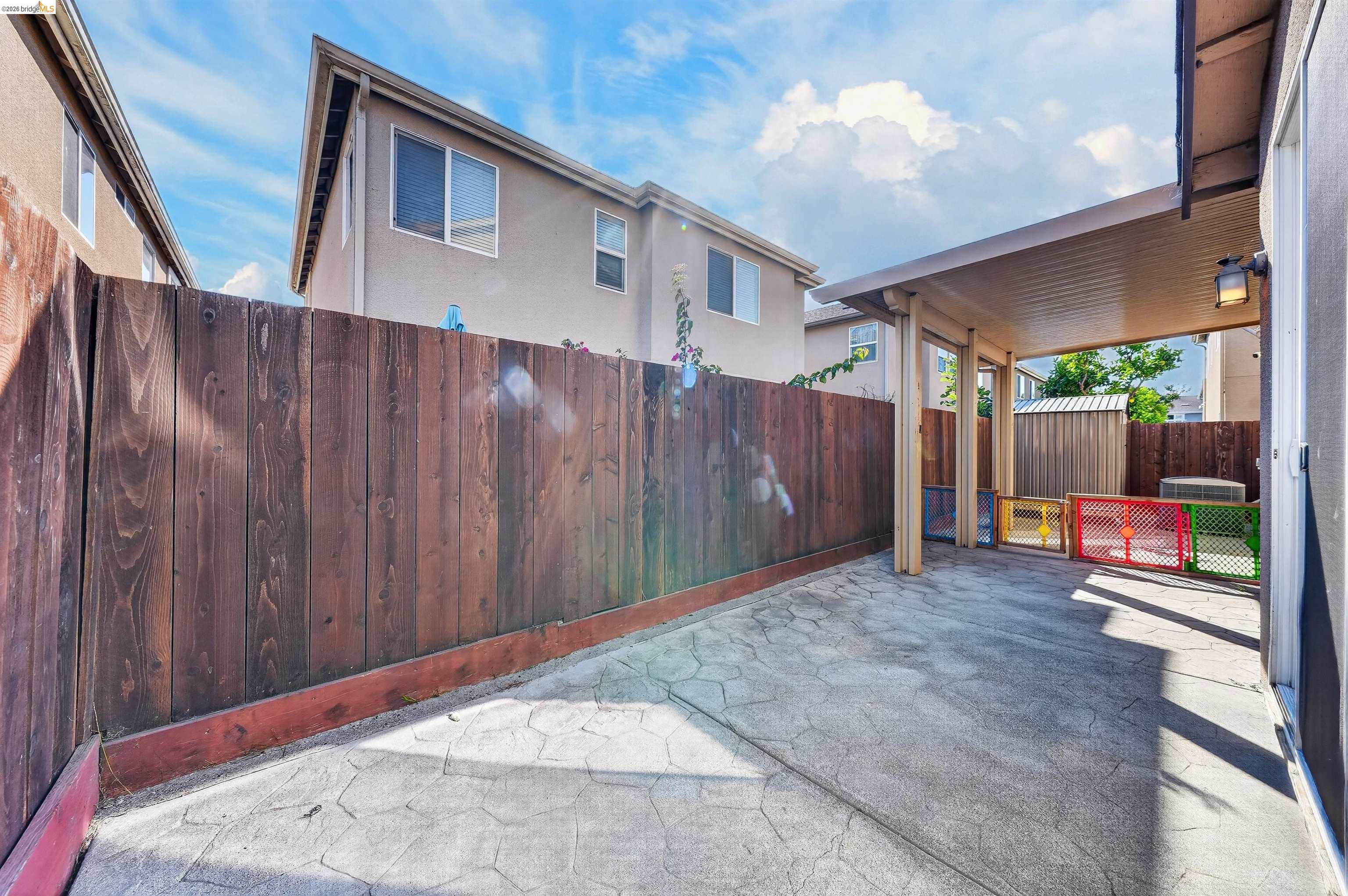 Paved backyard patio beneath a covered roof, enclosed by a tall wooden fence with colorful gates.