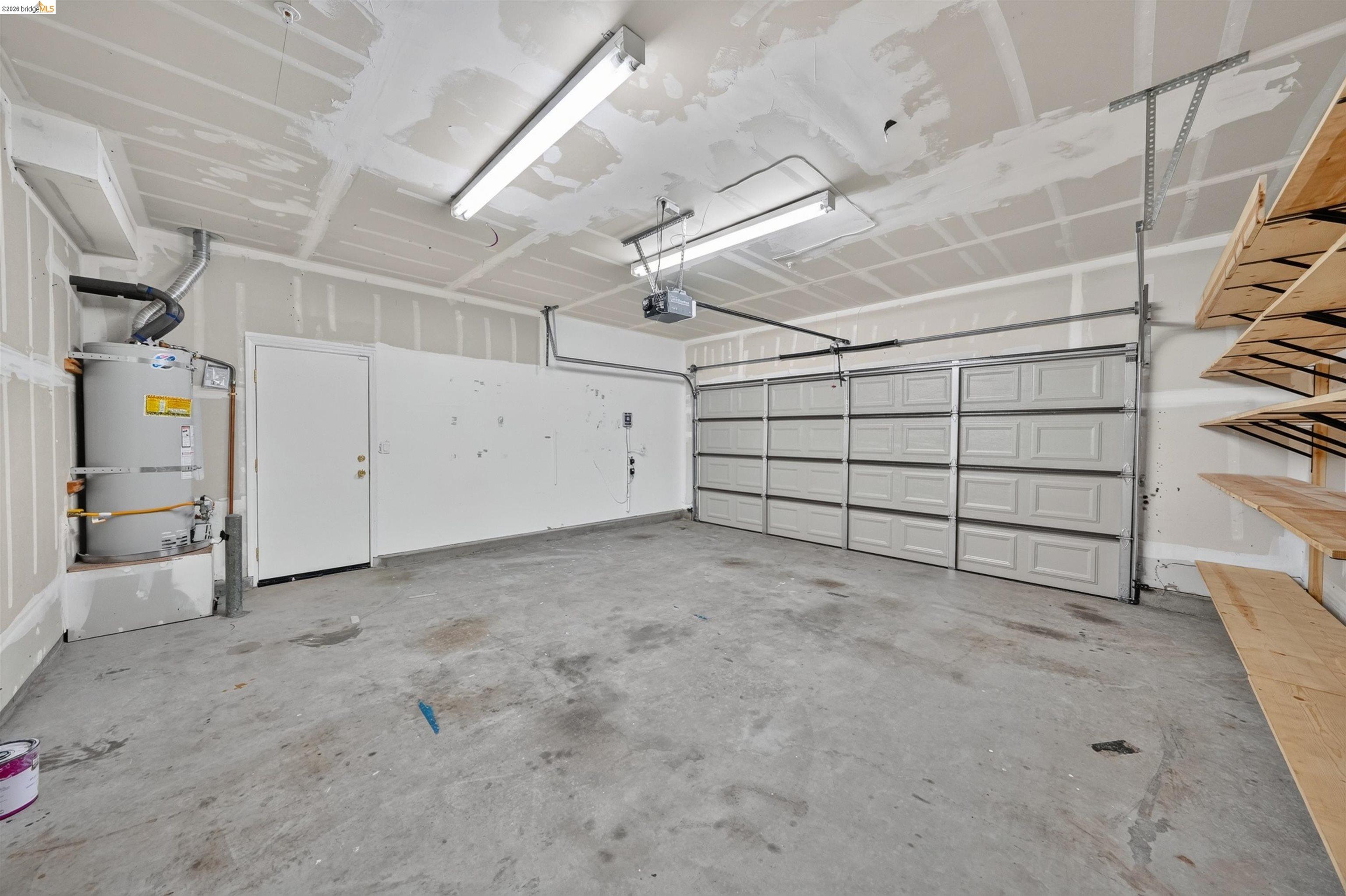 Unfinished garage with a wide sectional door, exposed drywall seams, and built-in wooden shelving.