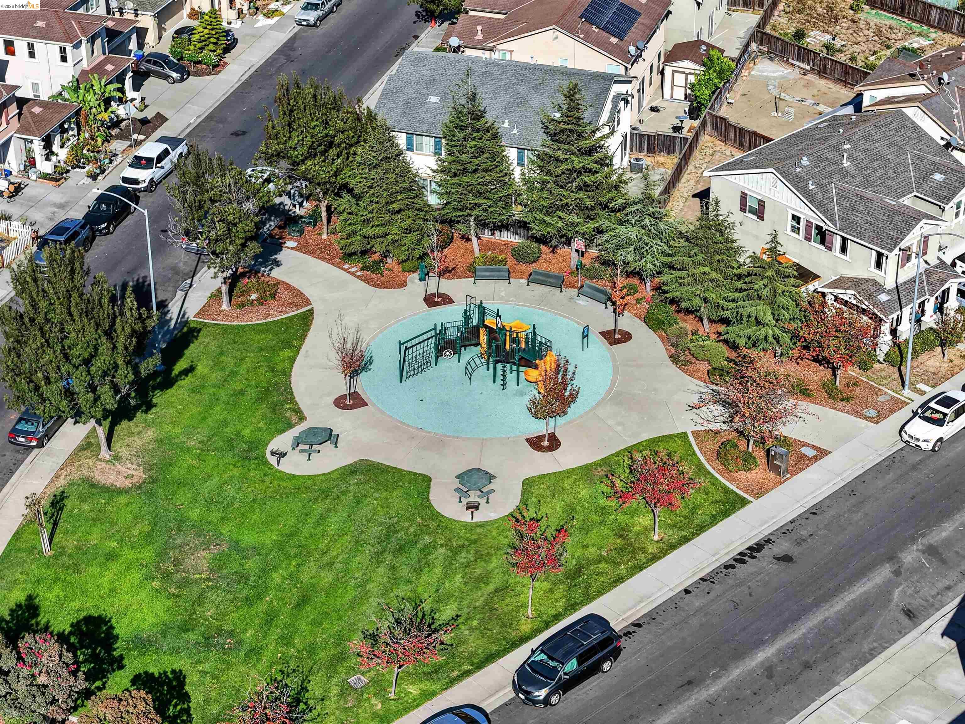 Aerial view of a neighborhood park with a circular playground, benches, and landscaped lawns.