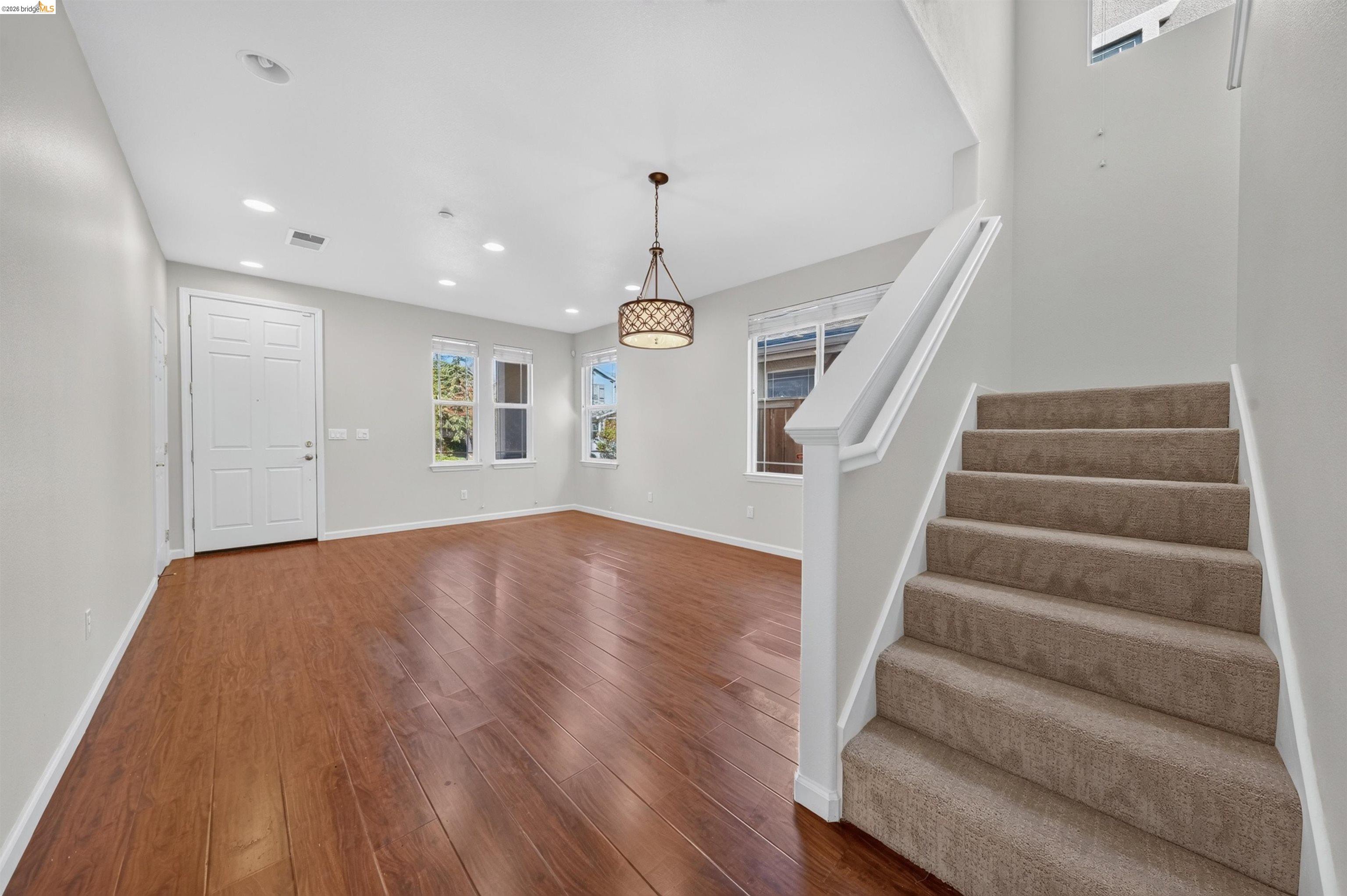 Open entry area with wood-look floors, a pendant light, and carpeted stairs.