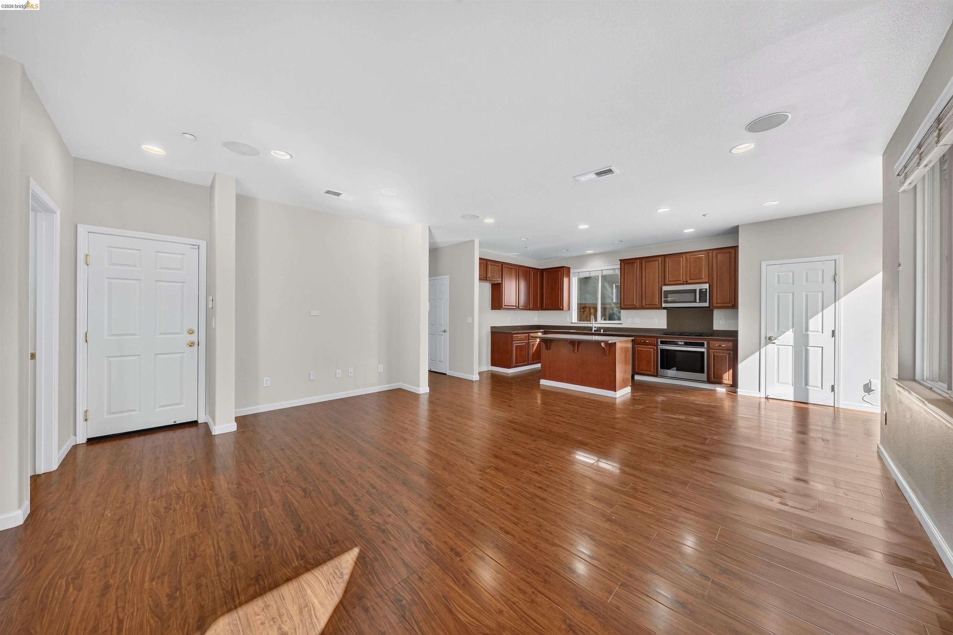 Open-plan kitchen and living area with hardwood floors, a central island, and reddish-brown cabinets.