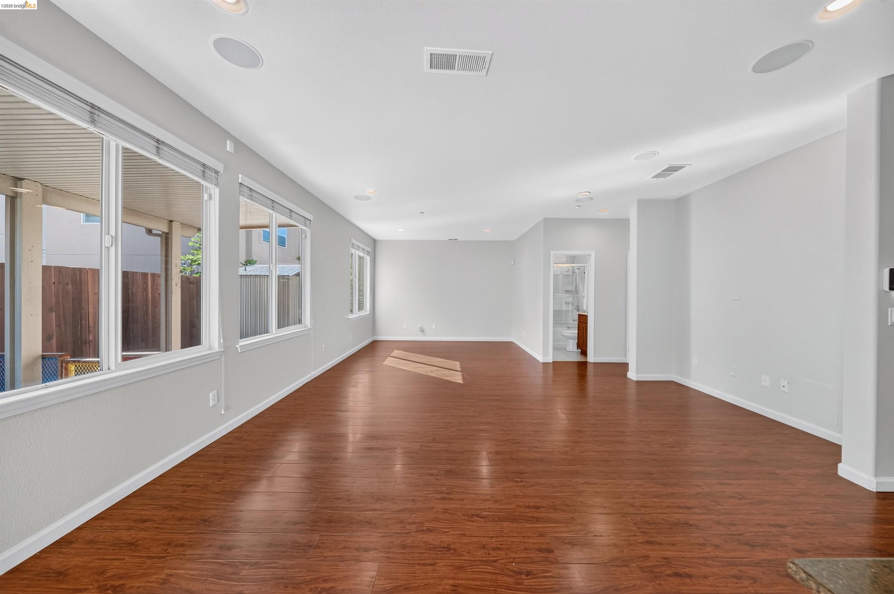 Empty living room with reddish-brown wood flooring and a wall of large windows.