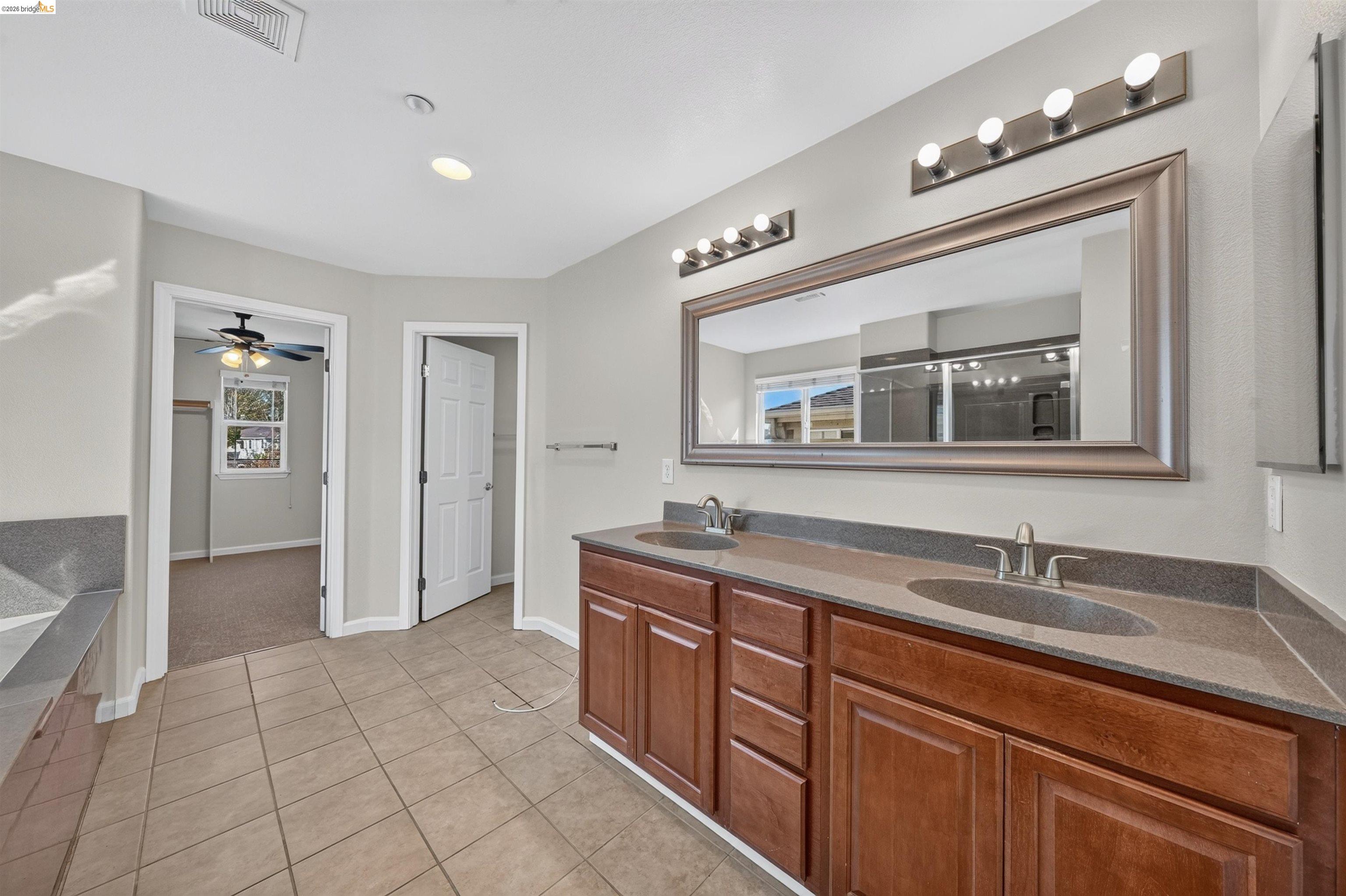 Bathroom with a long double-sink vanity, wood cabinets, and a large mirror.