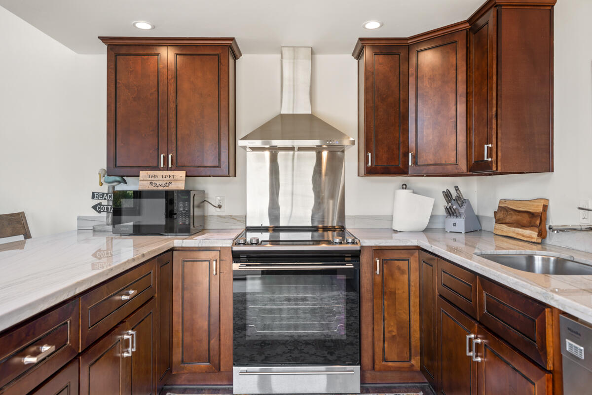 Kitchen with dark wood cabinetry, stone countertops, and a stainless steel range and hood.