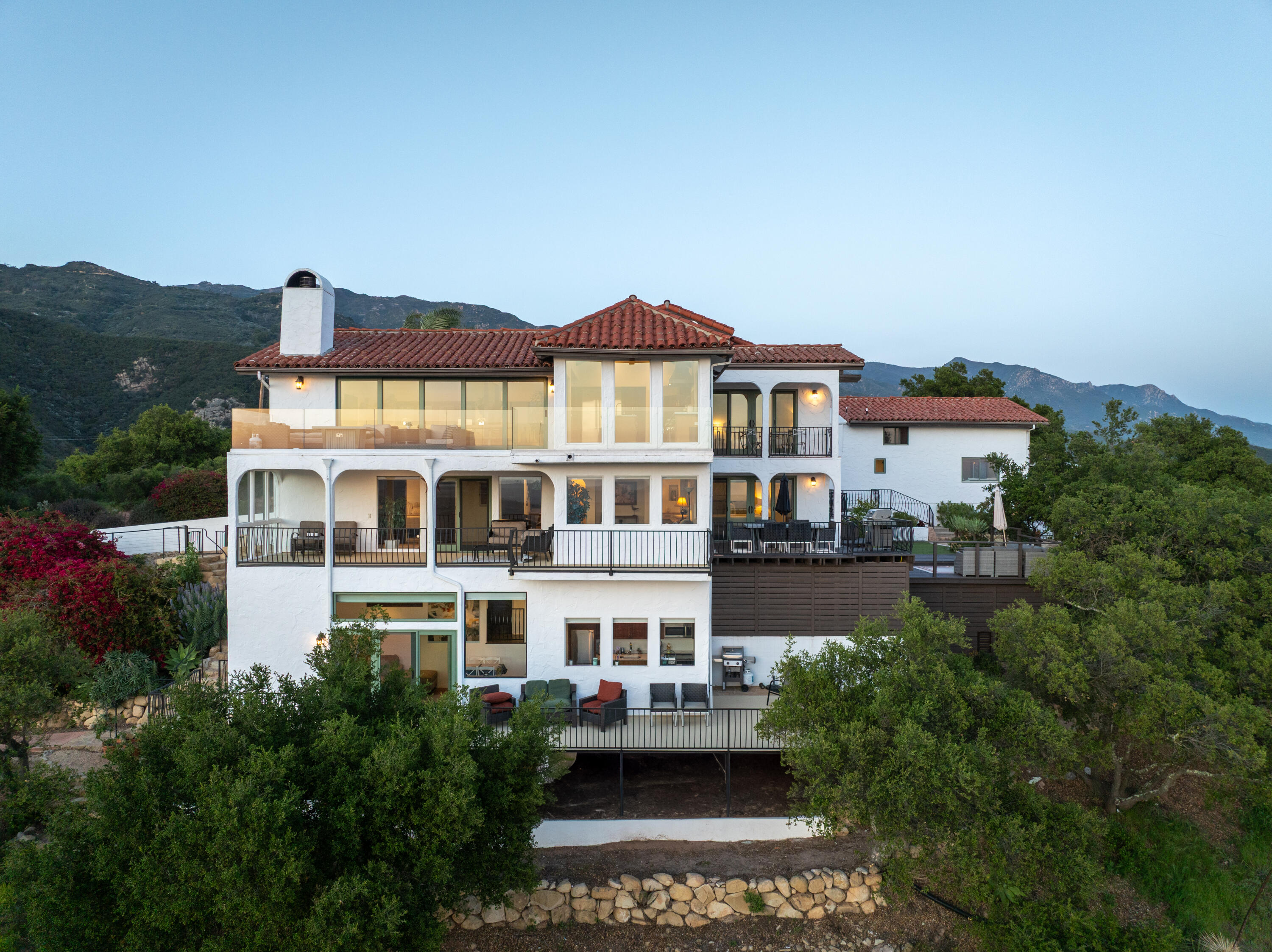 Multi-level white stucco home with red tile roofs, broad balconies, and mountain views.