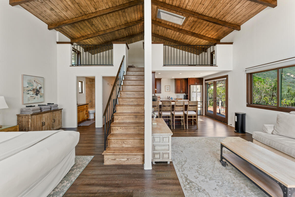Open-plan living room with a vaulted wood ceiling, central staircase, and kitchen opening to a garden.