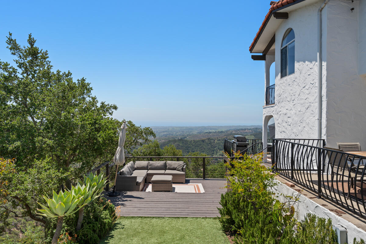 Outdoor deck with a sectional sofa and landscaped garden overlooking green hills.