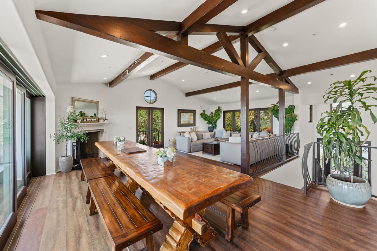 Open-plan dining and living room with exposed timber beams, a long wooden table, and a fireplace.