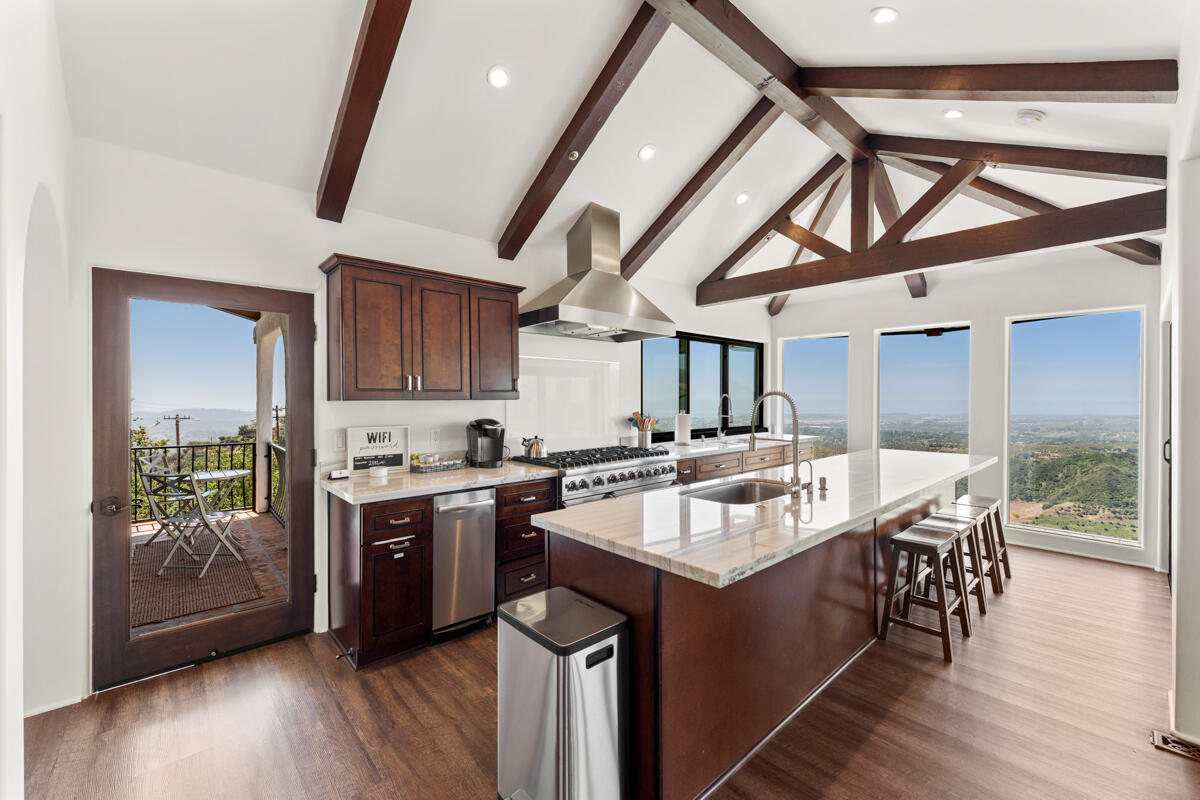 Kitchen with a marble-topped island, exposed wood beams, and windows overlooking rolling hills.
