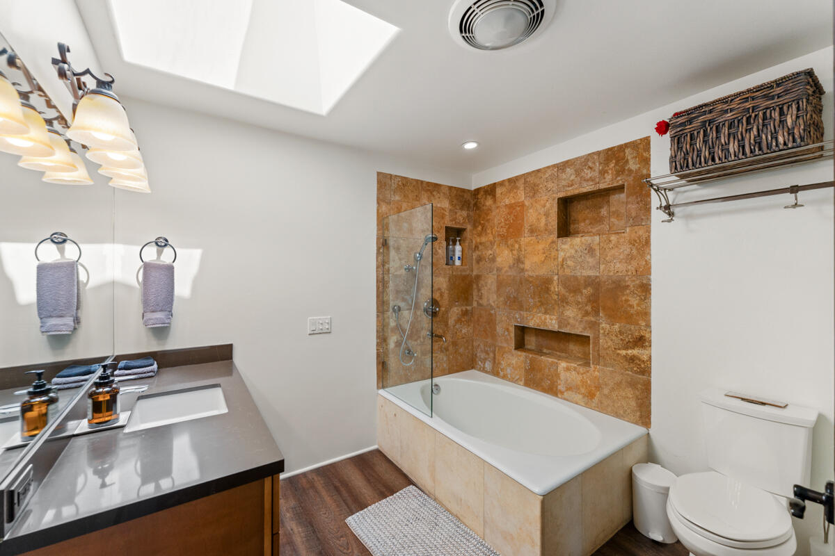 Bathroom with a stone-tiled tub and shower, gray-countertop vanity, and skylight.
