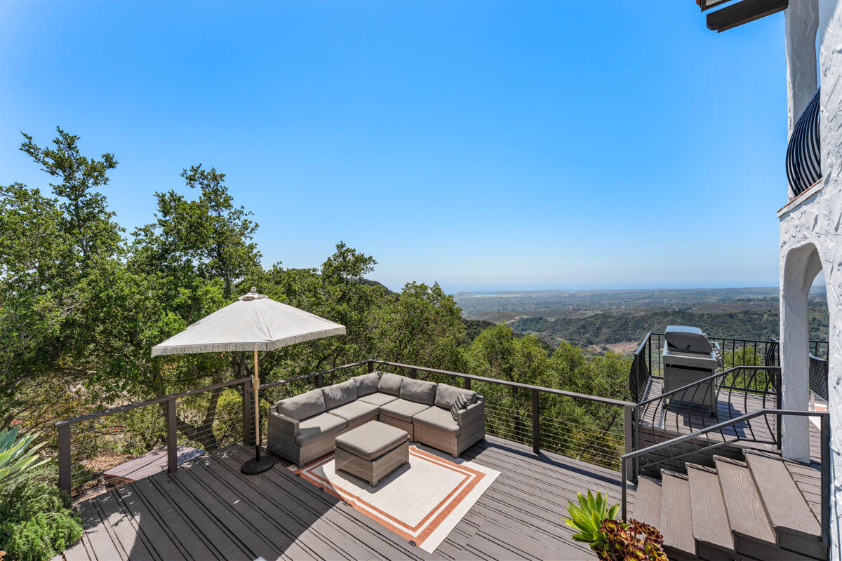 Furnished deck patio with sectional seating and umbrella overlooking wooded hills.