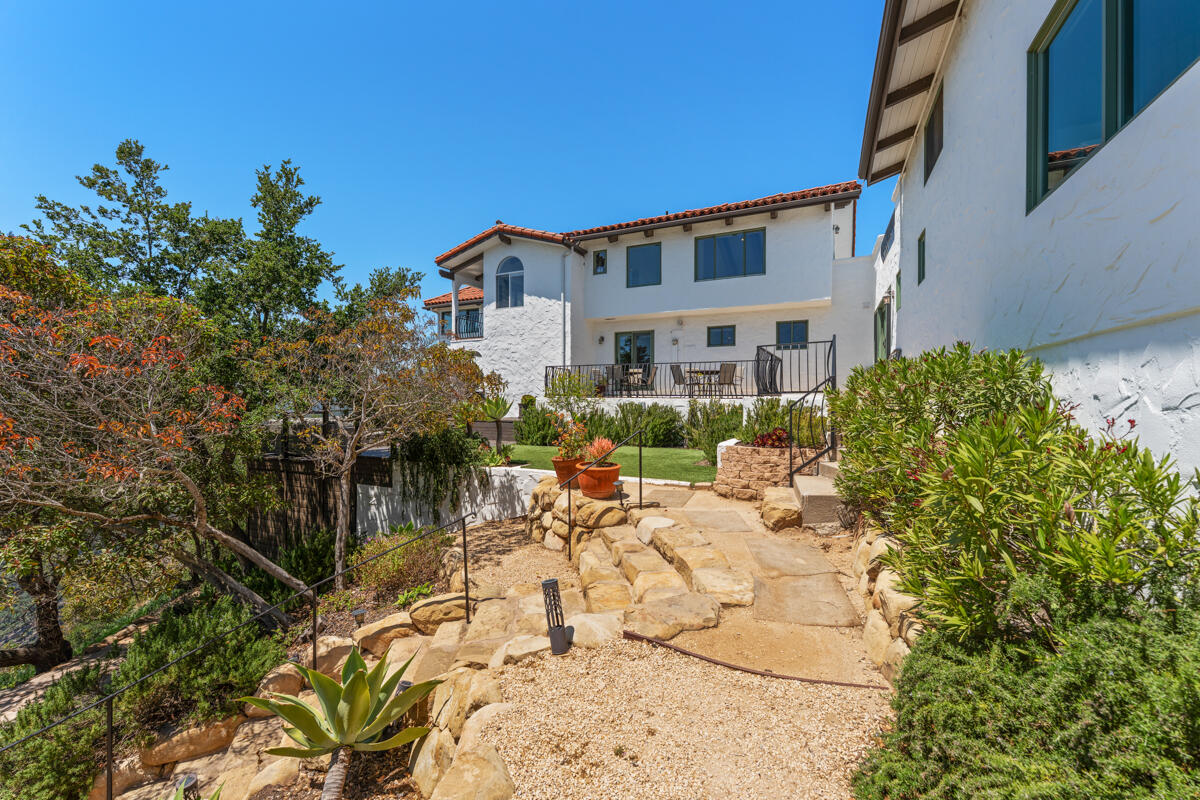 White stucco home with a red tile roof above stone garden steps and a raised patio.