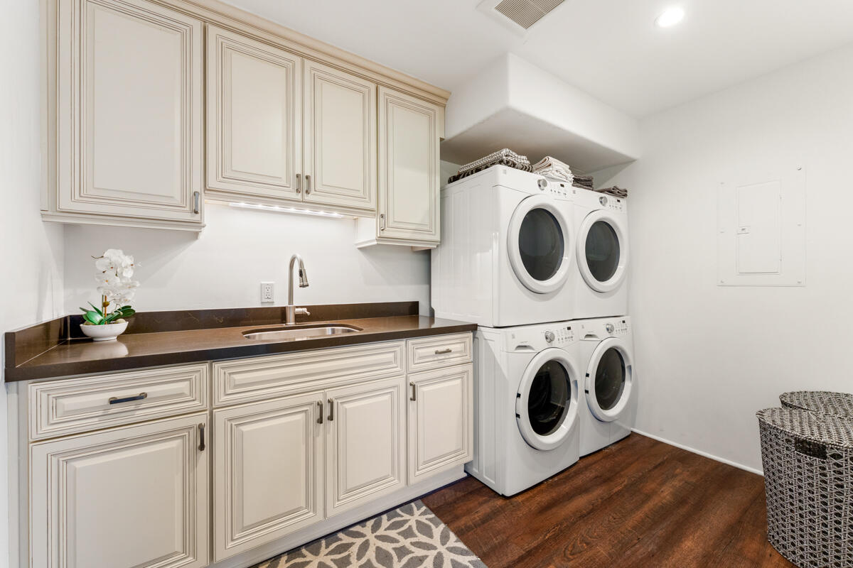 Laundry room with white cabinetry, a dark countertop and sink, and stacked front-loading washer and dryer.