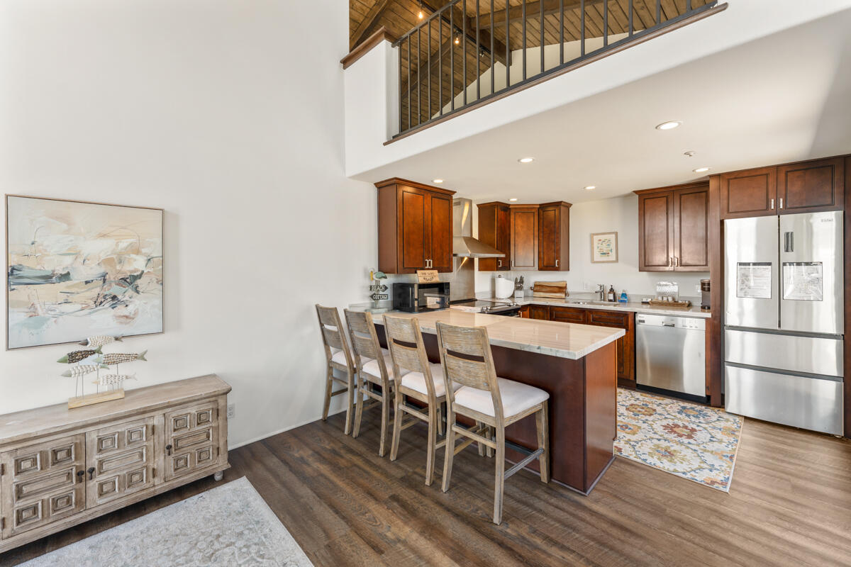 Kitchen with a large stone island, dark wood cabinets, stainless steel appliances, and an open loft above.