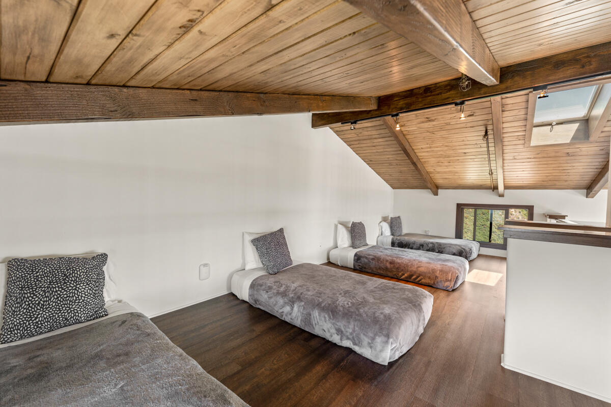 Attic bedroom with several low beds beneath a sloped wood-plank ceiling.
