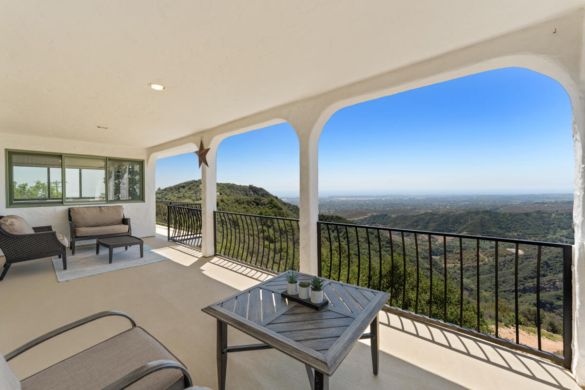 Covered arched terrace with outdoor seating and expansive views over green hills.