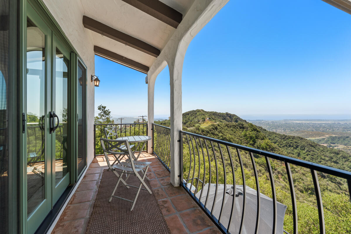 Covered balcony with a small table overlooking wooded hills and the distant coastline.
