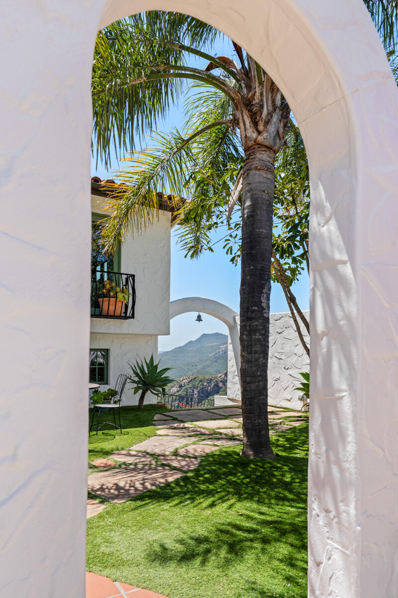 White stucco arch frames a palm-lined courtyard and mountain views.