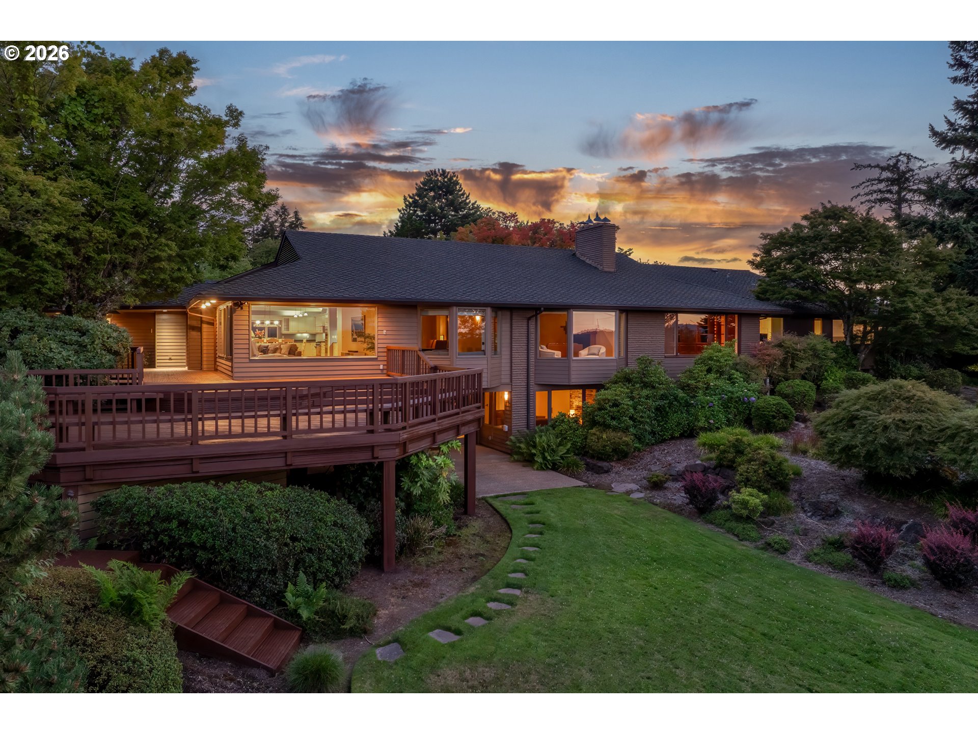 Home with a raised wooden deck and landscaped backyard at sunset.