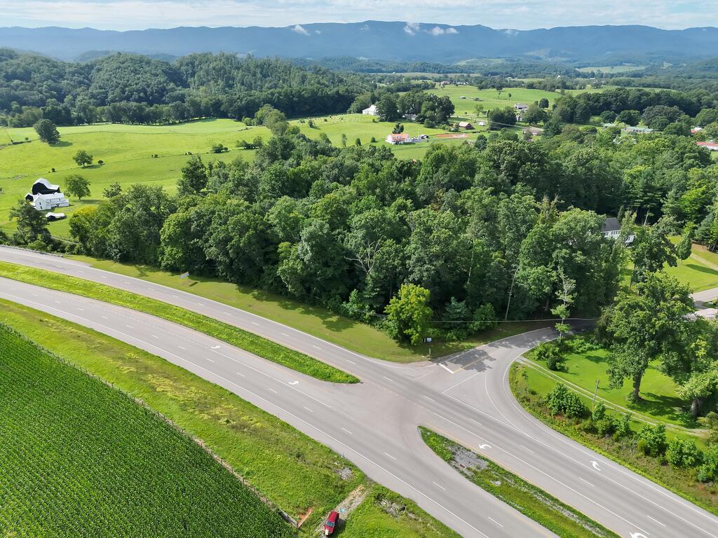 Aerial view of wooded land at a rural road intersection, with open fields and mountain ridges beyond.