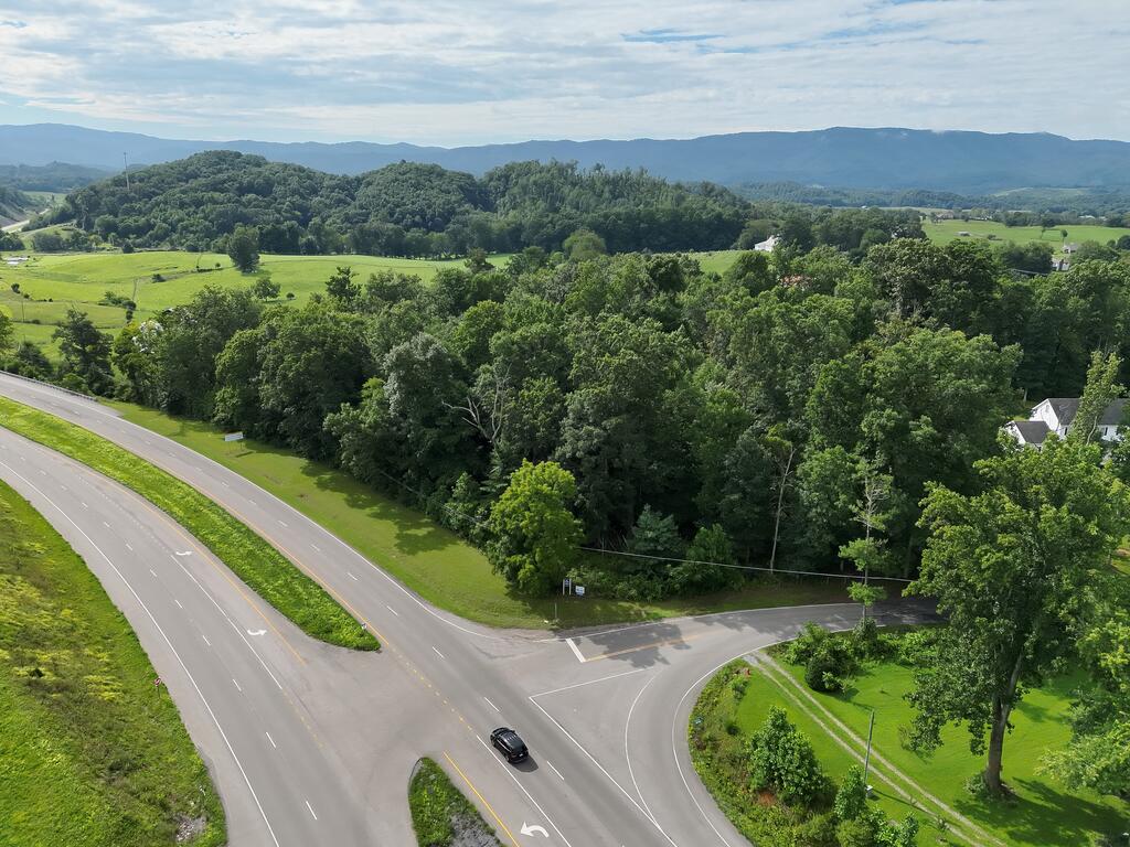Aerial view of wooded land beside a highway intersection, with open fields and distant mountains.