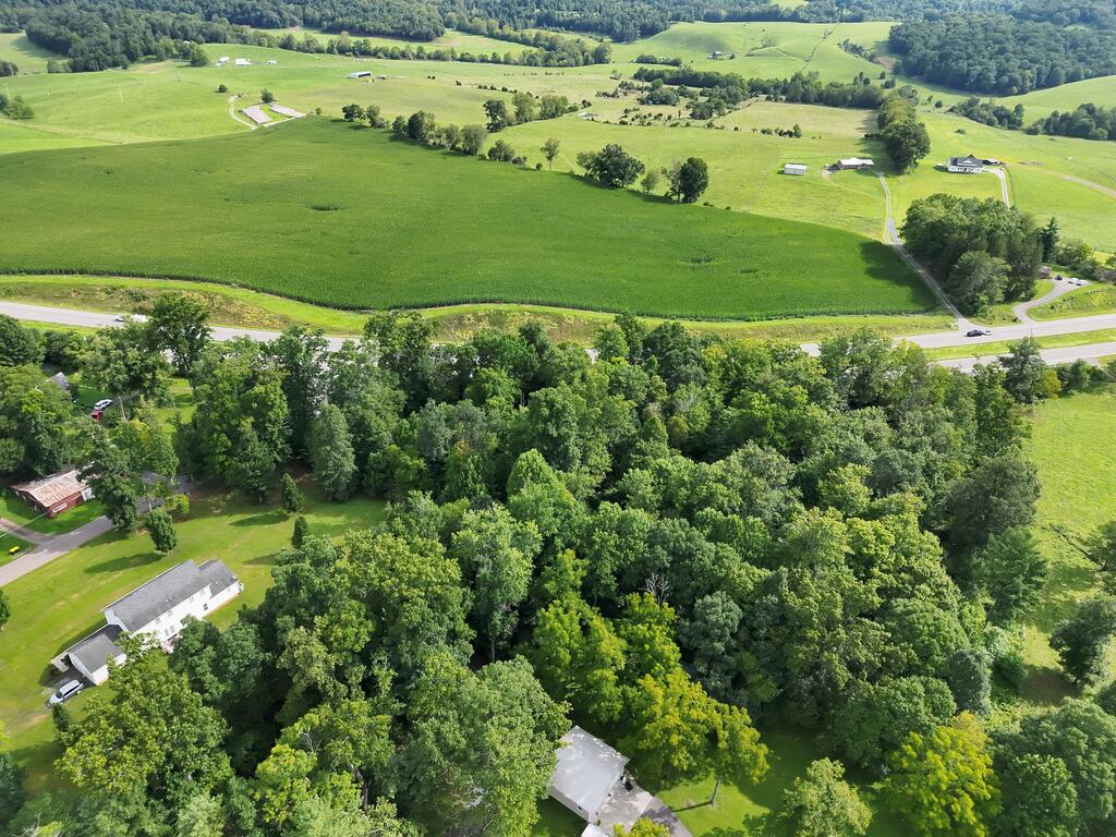 Aerial view of green rural acreage beside a road, bordered by woods and rolling fields.