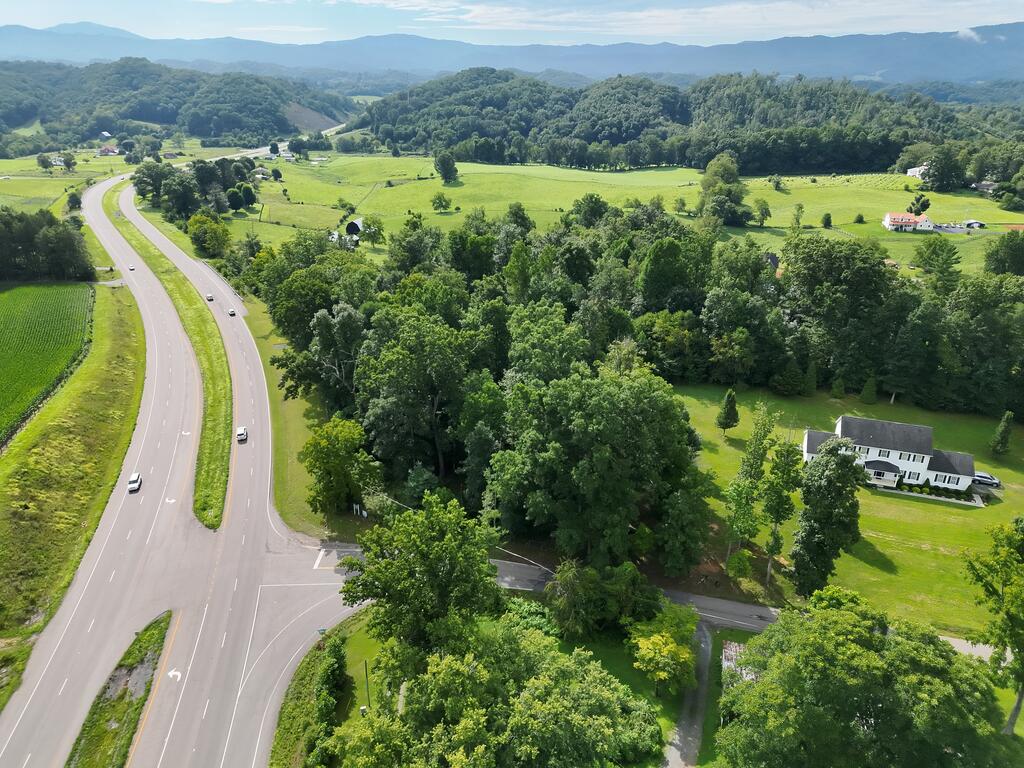 Aerial view of a divided highway through green fields and woods, with distant mountain ridges.