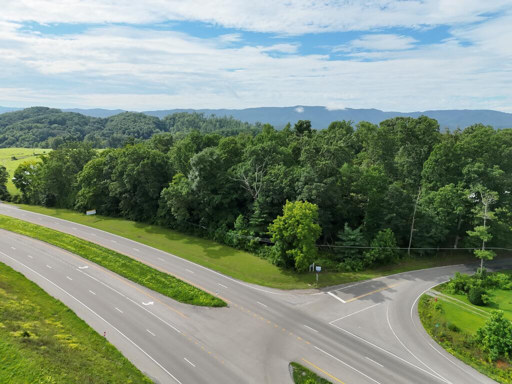 Vacant grassy land beside a highway intersection, with wooded hills and distant mountains.