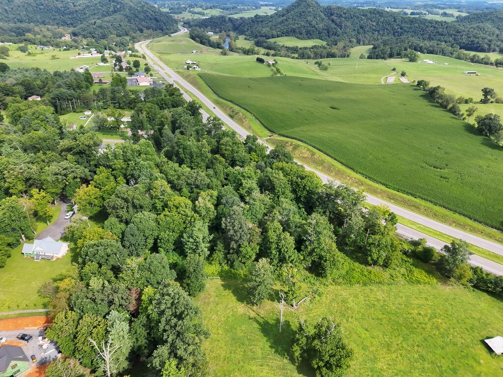 Aerial view of green fields beside a highway, with wooded hills and scattered homes.