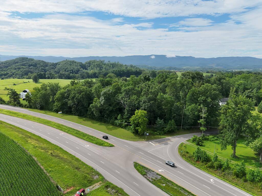 Aerial view of wooded land and fields beside a highway intersection, with distant mountain ridges.