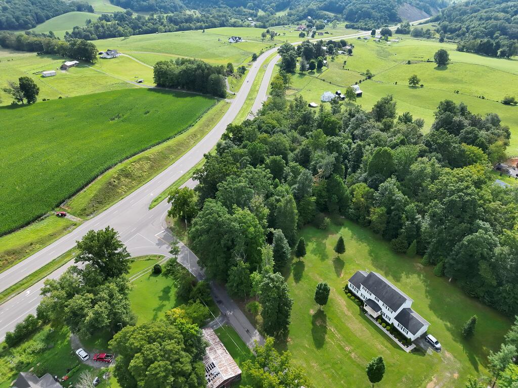 Aerial view of green rural land beside a highway intersection, with scattered homes and wooded hills.