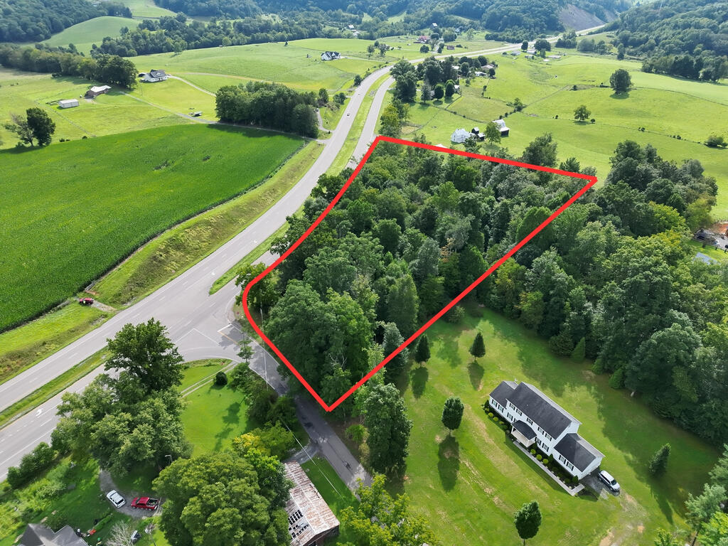 Aerial view of a wooded parcel outlined in red beside a road junction and open fields.