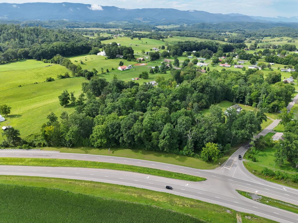 Aerial view of wooded acreage beside a highway, with farmland and mountains beyond.