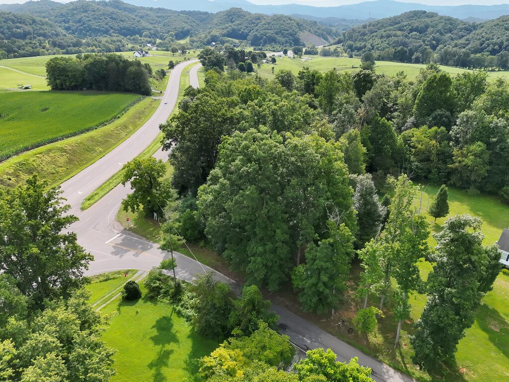 Aerial view of wooded vacant land beside a road intersection, with green fields and mountain ridges beyond.