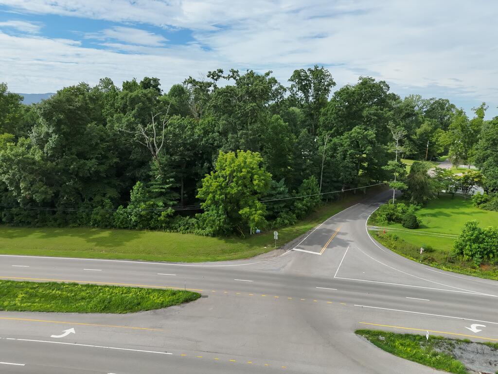 Aerial view of wooded land beside a road intersection, with grassy clearings and dense trees.