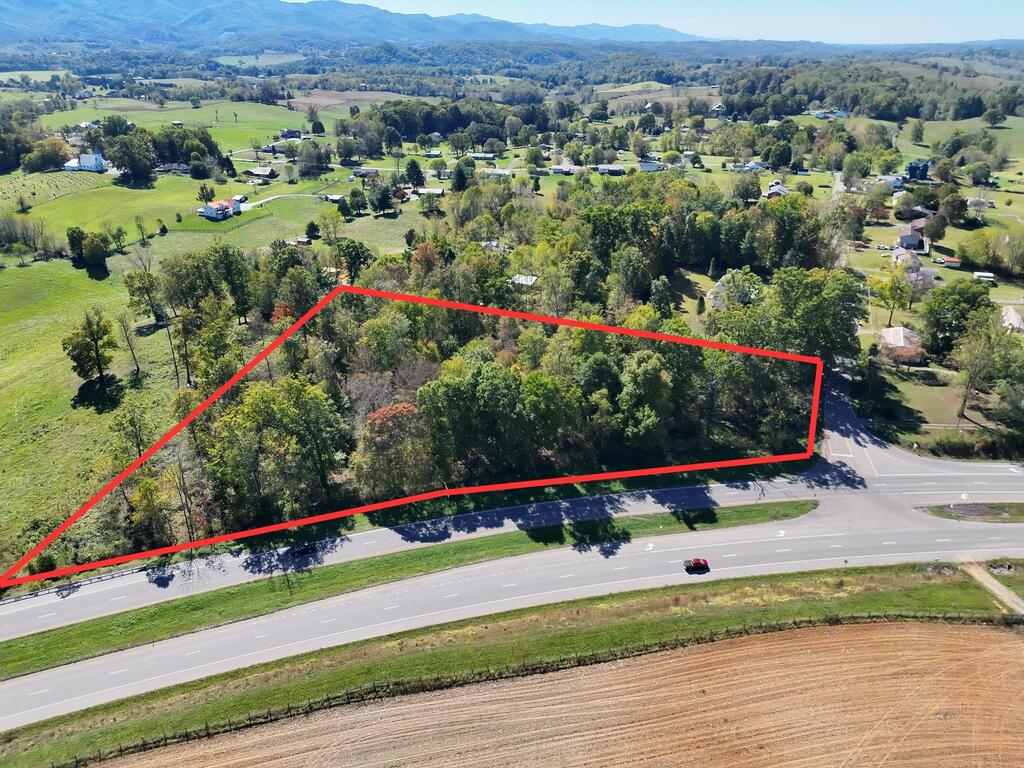 Aerial view of wooded land outlined in red along a divided highway, with mountains in the distance.
