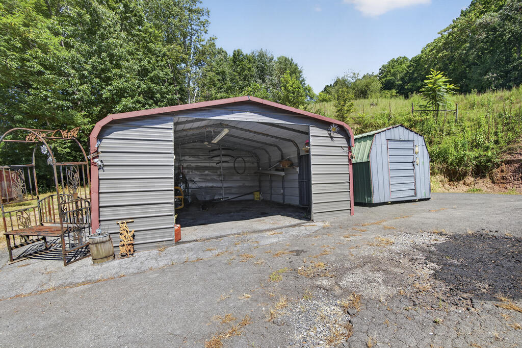 Open-front metal garage and smaller storage shed beside a paved driveway