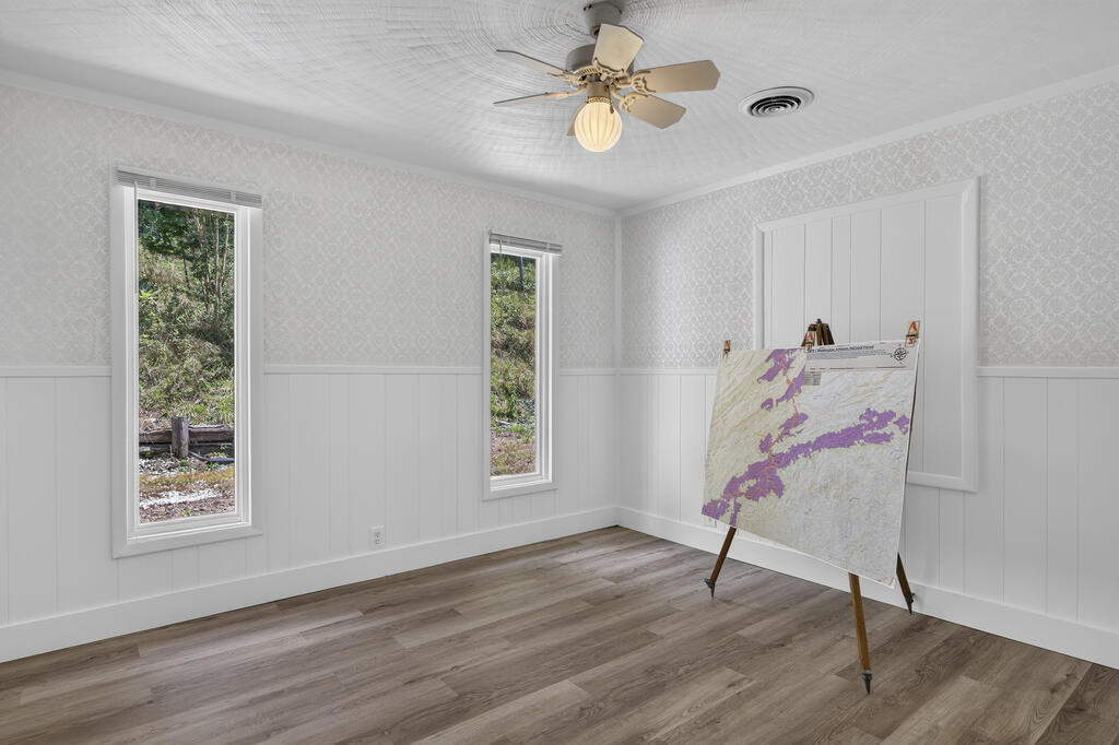 Empty room with gray flooring, white wainscoting, two windows, and a map on an easel.